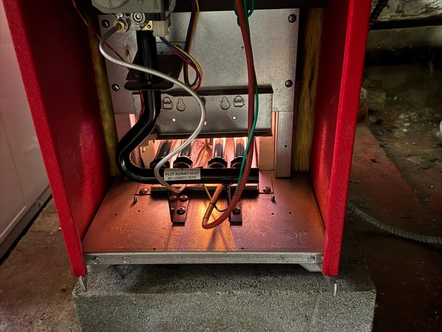 Red furnace with panel open showing warm glowing burners during a tune-up